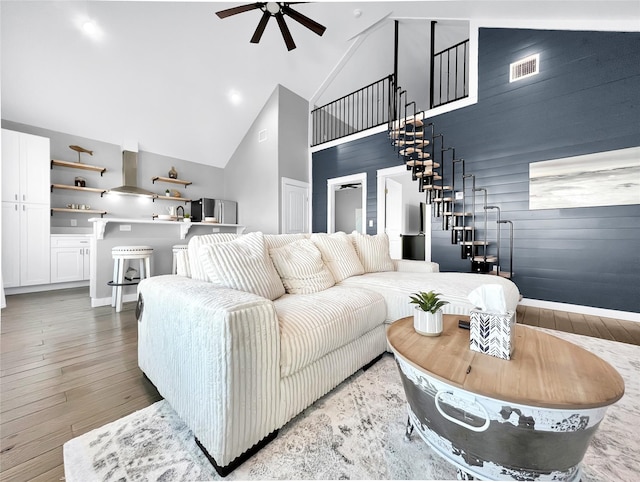 living room with wood-type flooring, wooden walls, ceiling fan, and high vaulted ceiling