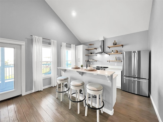 kitchen featuring wall chimney range hood, stainless steel refrigerator, a breakfast bar, wood-type flooring, and white cabinets