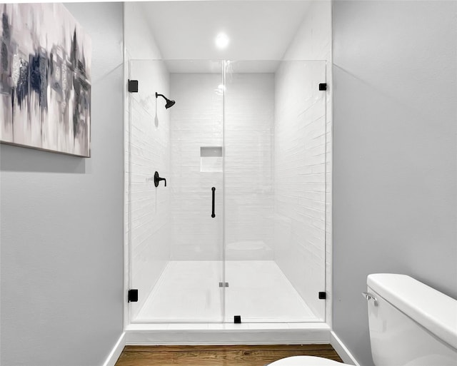 bathroom with wood-type flooring, a shower with shower door, and toilet