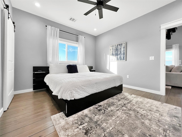 bedroom featuring hardwood / wood-style floors, a barn door, and ceiling fan