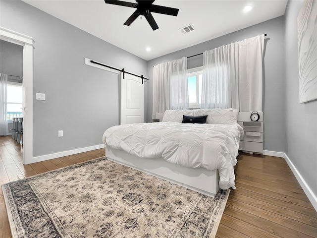 bedroom featuring ceiling fan, wood-type flooring, a barn door, and multiple windows