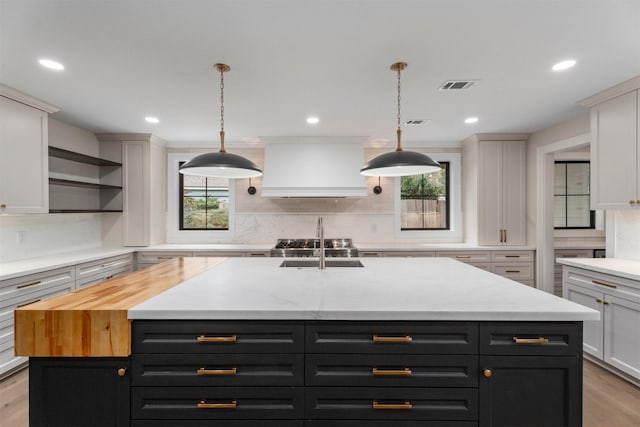 kitchen featuring custom exhaust hood, an island with sink, a healthy amount of sunlight, and white cabinetry