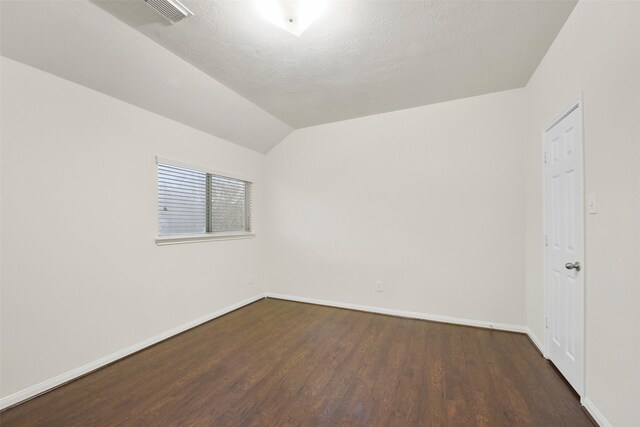 empty room featuring lofted ceiling, dark hardwood / wood-style floors, and a textured ceiling