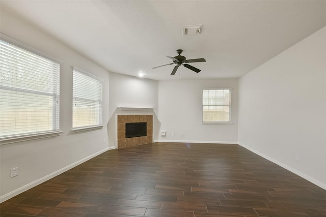 unfurnished living room with dark wood-style flooring, visible vents, a tiled fireplace, and a healthy amount of sunlight