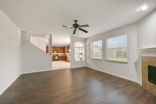 unfurnished living room with ceiling fan, dark hardwood / wood-style flooring, and a tiled fireplace