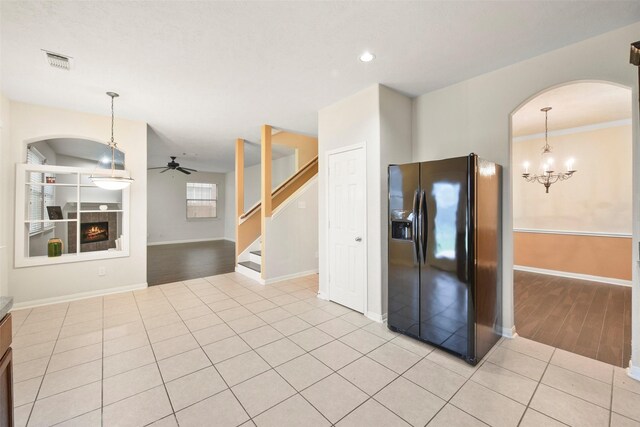 kitchen featuring light tile patterned flooring, decorative light fixtures, ceiling fan with notable chandelier, and black refrigerator with ice dispenser