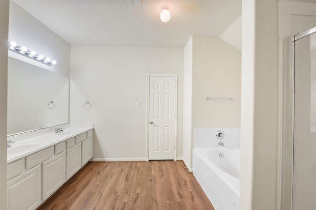 bathroom with double vanity, a garden tub, a sink, and wood finished floors