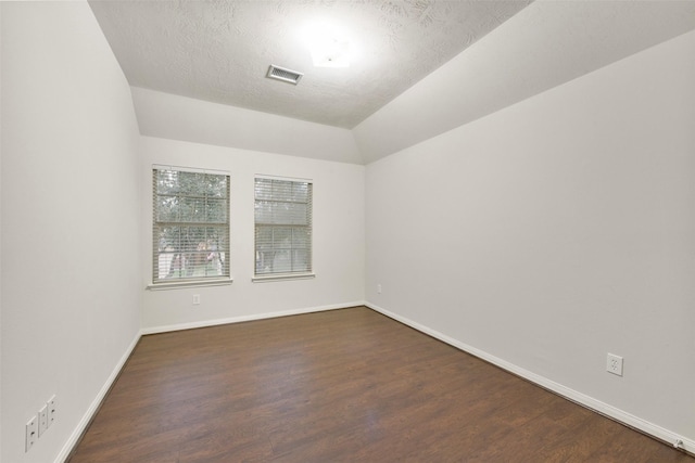 empty room with vaulted ceiling, dark wood-style floors, visible vents, and baseboards