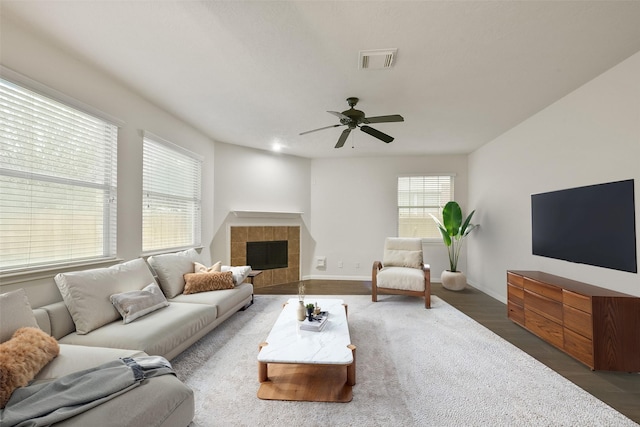 living room featuring dark wood finished floors, visible vents, a tiled fireplace, a ceiling fan, and baseboards