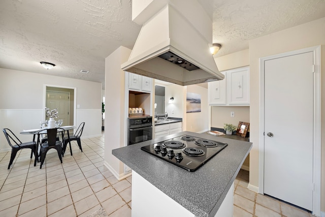 kitchen with light tile patterned floors, white cabinetry, island range hood, black appliances, and a textured ceiling