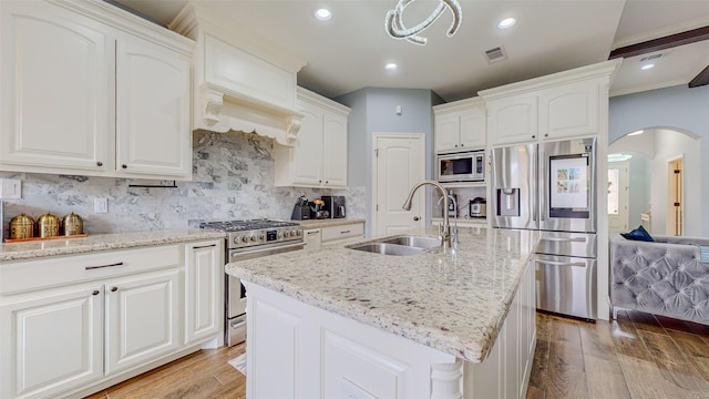 kitchen with appliances with stainless steel finishes, sink, white cabinets, a kitchen island with sink, and light stone countertops