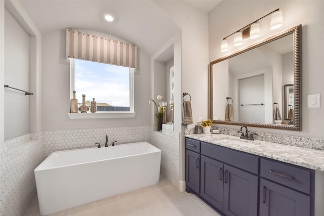 bathroom featuring vanity, a tub to relax in, tile patterned flooring, and tile walls