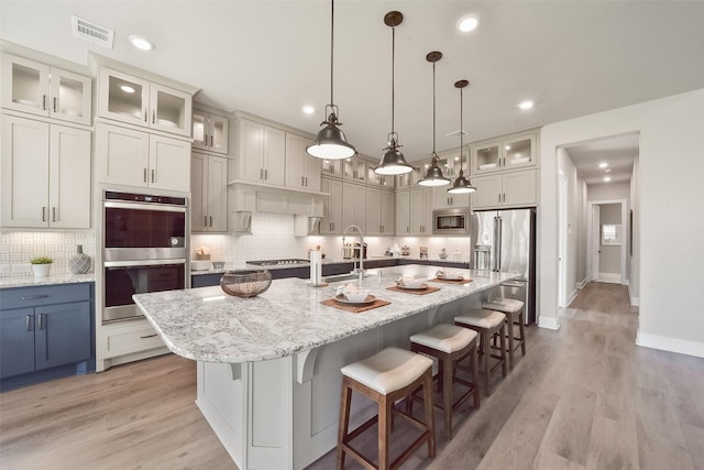 kitchen with appliances with stainless steel finishes, decorative light fixtures, decorative backsplash, light stone counters, and a center island with sink