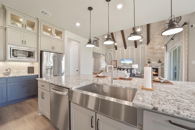 kitchen featuring hanging light fixtures, a large fireplace, stainless steel appliances, light stone countertops, and decorative backsplash