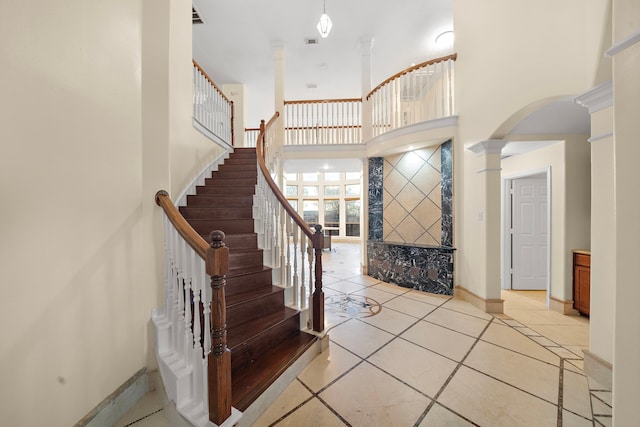 foyer featuring a towering ceiling, light tile patterned floors, and ornate columns