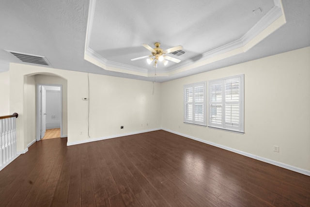 empty room with ceiling fan, ornamental molding, a tray ceiling, and dark hardwood / wood-style flooring