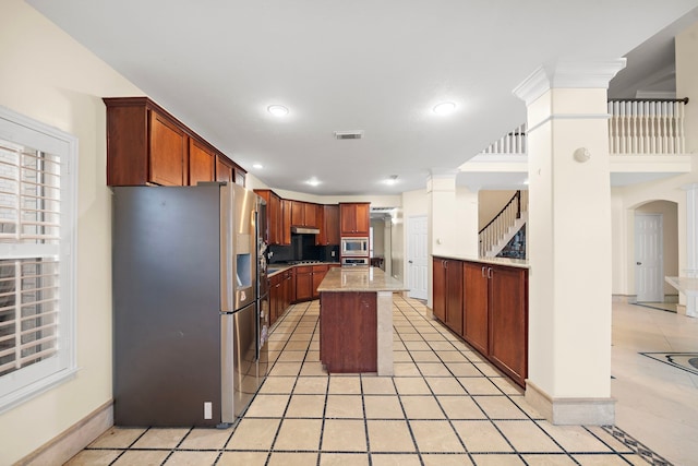 kitchen featuring stainless steel appliances, a kitchen island, light tile patterned floors, and decorative columns