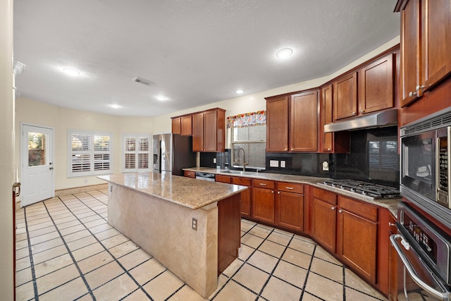 kitchen featuring a kitchen island, sink, backsplash, light stone counters, and stainless steel appliances