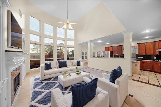 living room featuring light tile patterned flooring, a tile fireplace, a towering ceiling, ceiling fan, and decorative columns