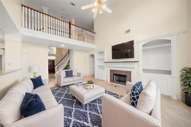 tiled living room with ceiling fan, built in features, and a high ceiling