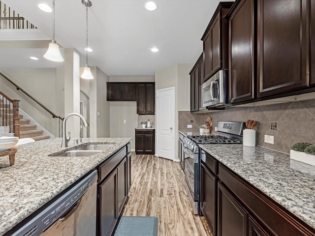 kitchen featuring sink, appliances with stainless steel finishes, backsplash, hanging light fixtures, and light stone countertops