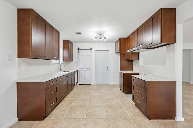 kitchen with tasteful backsplash, sink, light tile patterned floors, dark brown cabinetry, and a barn door