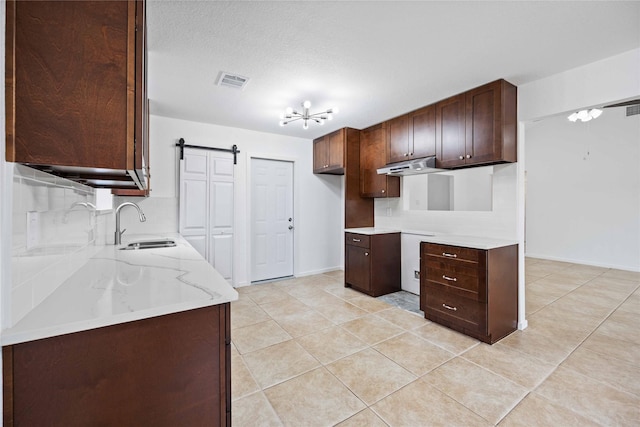 kitchen with sink, light tile patterned floors, light stone counters, decorative backsplash, and a barn door