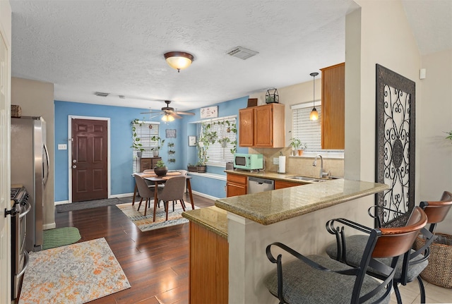 kitchen with appliances with stainless steel finishes, pendant lighting, sink, dark hardwood / wood-style flooring, and kitchen peninsula