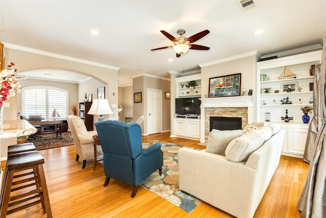 living room with a stone fireplace, light hardwood / wood-style flooring, ornamental molding, and ceiling fan