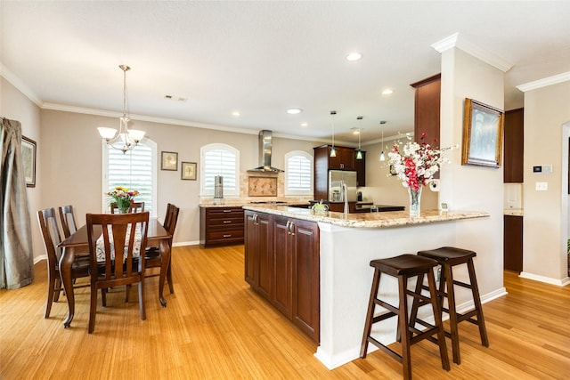 kitchen featuring hanging light fixtures, ornamental molding, a healthy amount of sunlight, and wall chimney exhaust hood