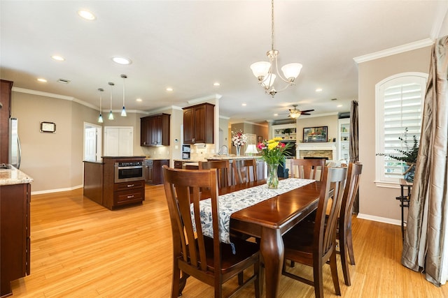 dining space with crown molding, ceiling fan with notable chandelier, a fireplace, and light wood-type flooring