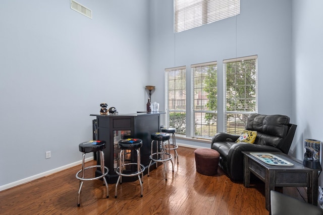 sitting room featuring hardwood / wood-style flooring, indoor bar, and a high ceiling