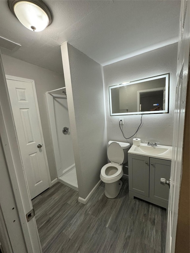 bathroom with hardwood / wood-style flooring, vanity, a textured ceiling, a shower, and toilet