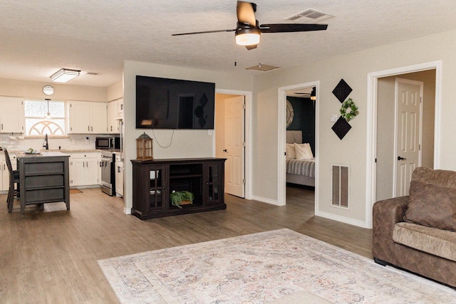 living room featuring ceiling fan, light hardwood / wood-style flooring, and a textured ceiling