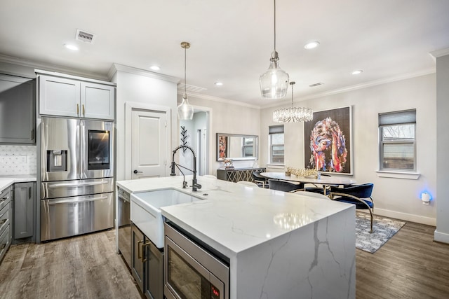 kitchen with sink, hanging light fixtures, a kitchen island with sink, stainless steel appliances, and light stone countertops