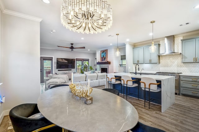 dining space featuring sink, ceiling fan with notable chandelier, wood-type flooring, and ornamental molding