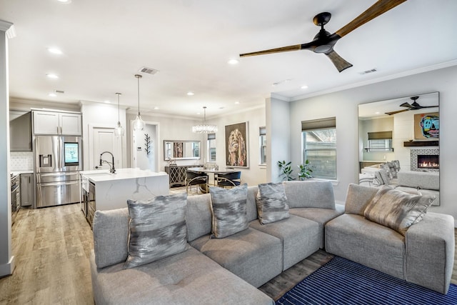 living room featuring sink, crown molding, light hardwood / wood-style flooring, and ceiling fan