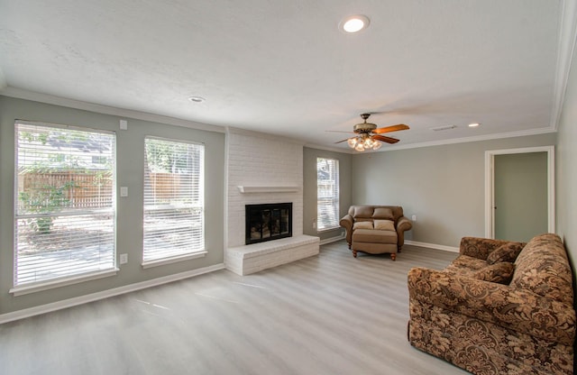 living room with crown molding, a brick fireplace, a healthy amount of sunlight, and light hardwood / wood-style floors