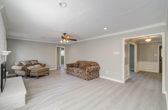 living room featuring ornamental molding, ceiling fan, a fireplace, and light hardwood / wood-style floors