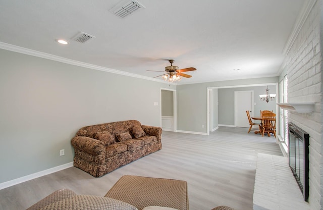 living room with crown molding, ceiling fan with notable chandelier, a fireplace, and light hardwood / wood-style flooring