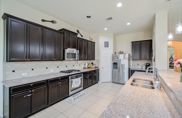 kitchen featuring appliances with stainless steel finishes, decorative light fixtures, tasteful backsplash, sink, and light stone counters