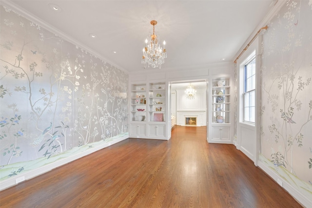 unfurnished living room with hardwood / wood-style flooring, ornamental molding, an inviting chandelier, and built in features