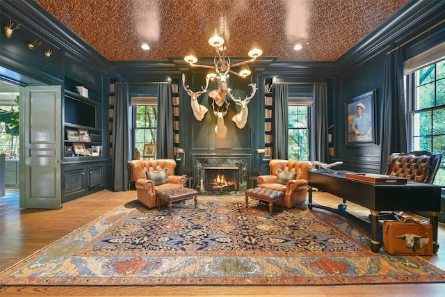 living area with a wealth of natural light, a decorative wall, crown molding, and wood finished floors