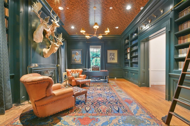 living area with crown molding, a notable chandelier, built in features, and hardwood / wood-style flooring