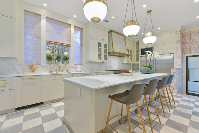 kitchen featuring pendant lighting, sink, a kitchen island with sink, light stone countertops, and custom exhaust hood