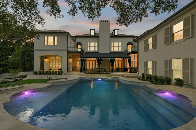 back house at dusk with a balcony and a patio