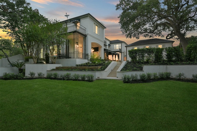 back house at dusk with a balcony and a yard