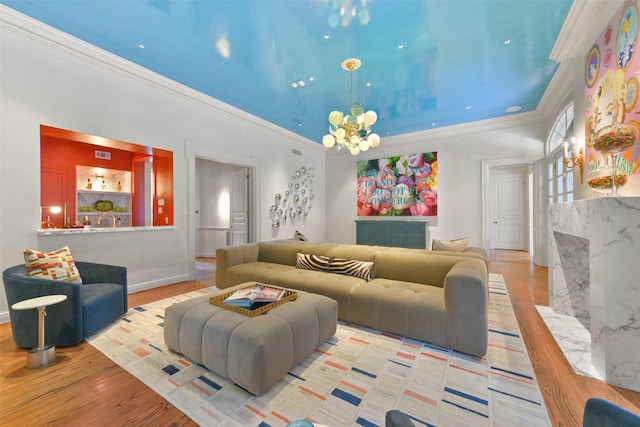 living room featuring an inviting chandelier, a high end fireplace, ornamental molding, and light wood-type flooring