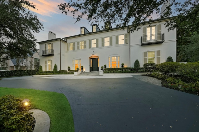 view of front of house featuring a balcony, a chimney, and stucco siding