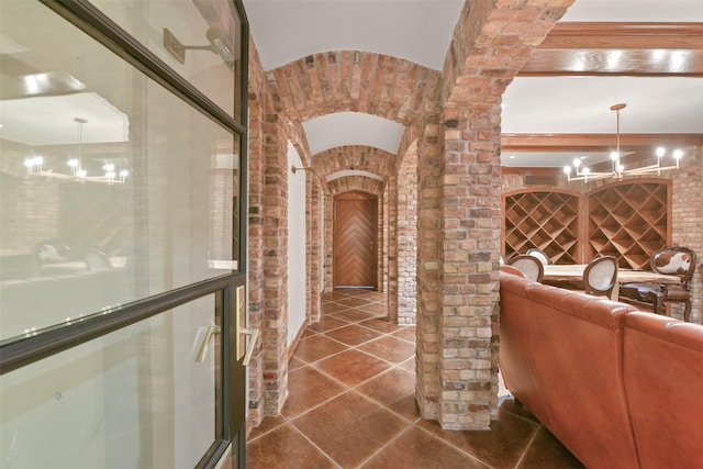 wine area featuring brick wall, dark tile patterned flooring, and a notable chandelier